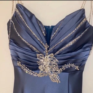 Mörkblå långklänning med pärldetaljer - Elegant mörkblå långklänning i satin med vackra diamant detaljer och draperad design. Perfekt för festliga tillfällen med sin glamorösa stil och smickrande passform. Passar både s och xs