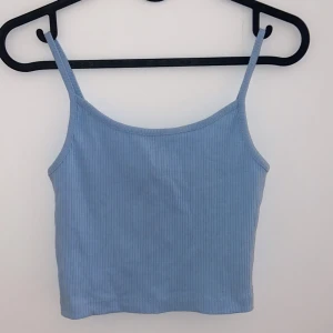 Ljusblå ribbad linnetopp - Säljer en superfin ljusblå ribbad linnetopp. Perfekt för sommardagar eller som ett lager under en kofta. Toppen är i ett mjukt och stretchigt material med smala axelband. Passar perfekt till både jeans och kjol!