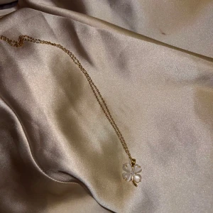 halsband med fyrklöverberlock - Säljer ett elegant halsband med en vacker fyrklöverberlock i genomskinligt material. Perfekt för att ge lite extra tur till din outfit! Kedjan är tunn och smidig, vilket gör den bekväm att bära hela dagen. Passar både till vardags och festliga tillfällen.