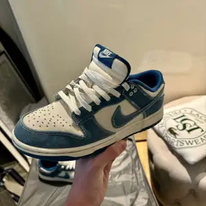 Säljer ett par snygga Nike Dunk sneakers i blått och vitt. De har en cool denim-look med vita snören och en klassisk Nike-logga på sidan. Perfekta för både vardag och fest! Skorna är i okej skick