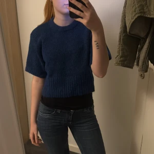 Mörkblå stickad tröja - Säljer en snygg mörkblå stickad tröja med korta ärmar. Perfekt för både höst och vår, och den har en ribbad kant vid ärmslut och nederkant. Tröjan är i bra skick och helt oanvänd☺️