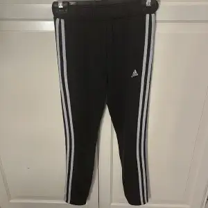 Säljer ett par svarta träningsbyxor från Adidas i storlek 13-14 år. Byxorna har de klassiska tre vita ränderna längs sidorna och är tillverkade i Primegreen-material. Perfekta för träning eller vardagsbruk!