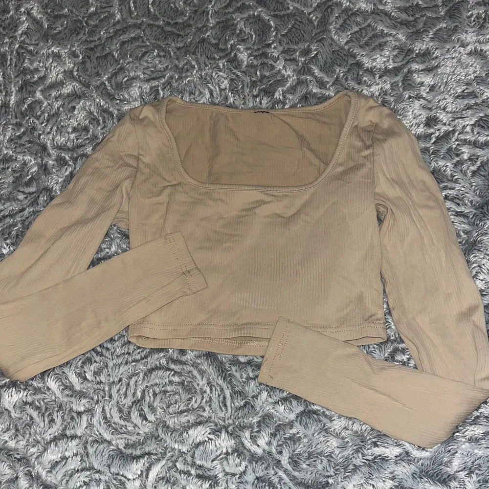 Säljer en superfin beige ribbad topp med långa ärmar. Den är croppad och har en fyrkantig halsringning som ger en stilren look. Perfekt för både vardag och fest! 🧡. Toppar.