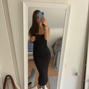 Svart ärmlös klänning - Snygg svart ärmlös klänning i tight passform. Perfekt för både vardag och festliga tillfällen. Klänningen är enkel och stilren, vilket gör den lätt att matcha med olika accessoarer.