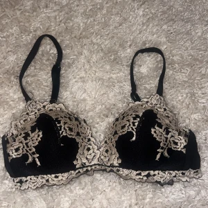 Intimissimi bh i svart - Snygg svart bh med vacker spetsdetalj i beige och blommönster. Den har justerbara axelband och en klassisk hakknäppning bak. Perfekt för en elegant look! Säljer den på grund av att den blivit för liten❤️