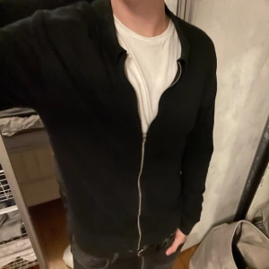 Svart full zip från Riley - Säljer en stilren svart kofta från Riley i storlek M. Perfekt för både vardag och fest. Perfekt att ha över en t-shirt eller skjorta! Säljer då den är lite väl liten på mig och har helt enkelt slutat använda den. Den har en mindre defekt på baksidan vilket syns i bilderna, den syns dock inte när du har på dig tröjan. För några frågor eller fler bilder skriv gärna!