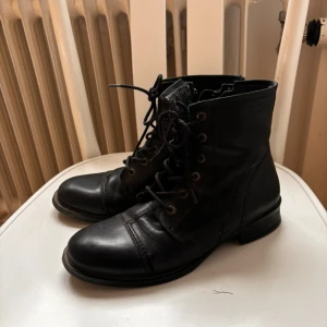 Svarta skinn boots med snörning - Säljer ett par svarta boots i skinn med snörning framtill. De har en klassisk design och ser ut att vara i bra skick. Perfekta för höst och vinter, och de passar till både vardag och lite mer uppklädda tillfällen.