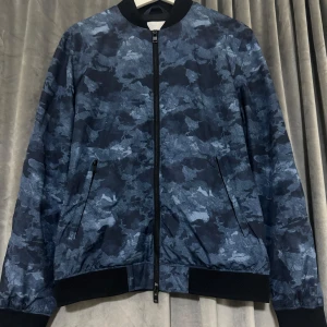 Blå camouflage bomberjacka från J.Lindeberg - Säljer en snygg blå camouflage bomberjacka från J.Lindeberg i storlek M. Jackan har en dragkedja framtill och ribbstickade muddar vid ärmslut och nederkant. Perfekt för höst och vår! 🧥