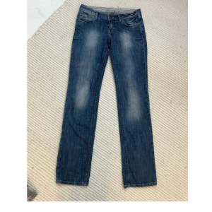 Blå jeans med coola bakfickor - Säljer ett par snygga blå jeans i bra skick. Bakfickorna är broderade med ett unikt och coolt mönster. Midjemåttet: ca 82cm Innerbenslängden: ca 87cm