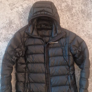 Svart dunjacka från Peak Performance - Säljer en svart dunjacka från Peak Performance i mycket bra skick. Jackan har en praktisk huva och dragkedja framtill. Perfekt för kyliga dagar och håller dig varm och bekväm. Passar både till vardags och utomhusaktiviteter.