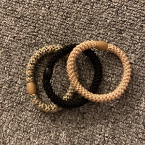Set med tre elastiska hårband - Säljer ett set med tre elastiska hårband i olika färger. Ett beige, ett svart och ett i kamouflagefärger. Perfekta för att hålla håret på plats eller som armband. De är gjorda av slitstarkt material och har en liten plastdetalj för extra stil. Passar både till vardag och fest (säljer alla 3 tillsammans för 11kr). 