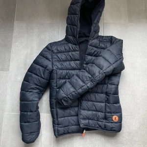 Svart pufferjacka från Save the Duck - Säljer en svart pufferjacka från Save the Duck, stl 14. Passar långd ca 150–160. Jackan är i bra skick med några små märken. Använd en säsong. Perfekt för kyliga dagar. Jackan är vändbar och både stilren och funktionell. Passar perfekt för höst och vinter!