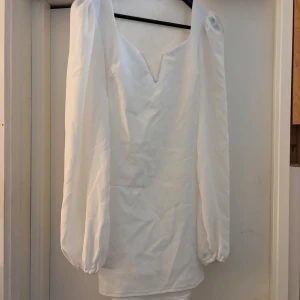 Vit klänning från NLY One - Säljer en elegant vit klänning från NLY One i storlek S. Klänningen har långa ärmar och en v-ringad design. Perfekt för vår- och sommarfester! Den är i bra skick med en liten fläck på framsidan.
