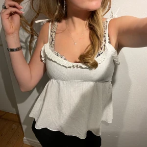 Vit ärmlös topp med volang - Säljer en söt vit ärmlös topp volangkant. Toppen har smala axelband och en luftig passform, perfekt för sommardagar. Den är i mycket bra skick och passar både till vardags och fest.