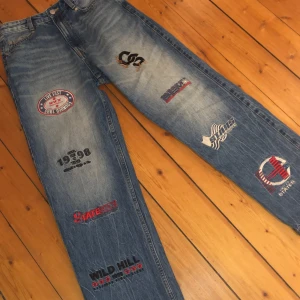 Jeans med tryck - Säljer ett par coola blåa jeans med olika tryck och broderier som 'STAY TRUE' på baksidan. De är baggy i passform och är perfekta för en casual och lite extra cool look. Jeansen har en vintage känsla och är nästan inte använda alls. Storlek EUR36, skulle säga cirka 30 i midjan och 32 i längd.