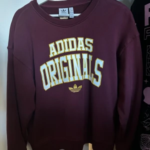 Vinröd sweatshirt från Adidas Originals - Säljer en snygg vinröd sweatshirt från Adidas Originals. Den har ett stort tryck i gult och vitt på framsidan. 