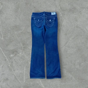 True religon Blå bootcut jeans - True religon Säljer ett par snygga blå bootcut jeans med vita sömmar. De har en klassisk femficksdesign och är perfekta för både vardag och fest. Jeansen är i bra skick och har en bekväm passform. Perfekta för dig som vill ha en tidlös stil!