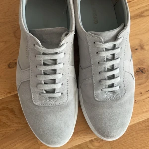 Grå sneakers från Axel Arigato - Ett par stilrena grå sneakers från Axel Arigato i mocka. De har snörning och en vit sula. Perfekta för både vardag och festliga tillfällen. Skorna är i mycket bra skick och redo för nya äventyr! De har använts  väldigt få gånger och har inte utsatts för regn. Inga funktionsdefekter. 