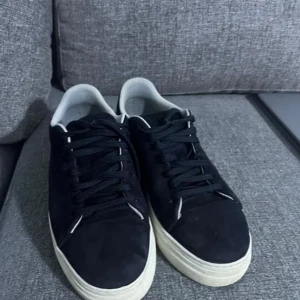 Svarta sneakers från Selected homme  - Snygga svarta sneakers från Selected Homme i mocka med vita sulor. Skorna har klassisk snörning och en stilren design som passar perfekt till vardags. Tillverkade i Portugal.