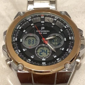 Silverfärgad klocka från Paterson - Snygg och robust klocka från Paterson med silverfärgad länk och svart urtavla. Klockan har både analog och digital visning samt kronograf-funktion. Den är vattentät upp till 30 meter och har en sportig design med tydliga markeringar och detaljer.