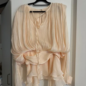 Glansig volang Klänning S/M  - Beige/aprikos/champagne klänning storlek M men passar S/M sååå fin klänning men blev tyvärr för kort på mig som är 175, rekommenderar till någon som är lite kortare. Oanvänd, kan skicka fler bilder vid intresse.  Kan gå ner i pris vid snabb affär 