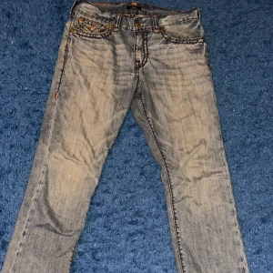 Blå jeans från True Religion - Snygga blå jeans från True Religion med klassisk femficksdesign och kontrastsömmar. De har en knappgylf och märkeslogga på bakfickan. Perfekta för en avslappnad stil. Köpta på bestsecret för 3499. Pyttelite heeldrag men knappt något som syns.