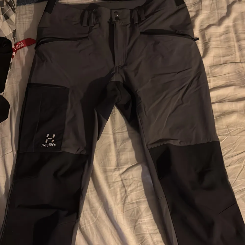 Säljer ett par grå och svarta byxor från Haglöfs. Byxorna har en praktisk design med flera fickor och dragkedja. Perfekta för utomhusaktiviteter med slitstarkt material. Helt nya inget fel alls köpt för 2000 på Intersport . Farkut & Housut.