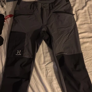 Grå och svarta byxor från Haglöfs - Säljer ett par grå och svarta byxor från Haglöfs. Byxorna har en praktisk design med flera fickor och dragkedja. Perfekta för utomhusaktiviteter med slitstarkt material. Helt nya inget fel alls köpt för 2000 på Intersport 