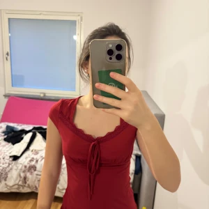 Röd topp med spetsdetaljer - Säljer en röd topp med spetsdetaljer och knyt framtill. Toppen har korta ärmar och en figurnära passform. Perfekt för en stilren look.