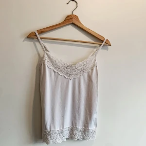 Vit linnetopp med spetsdetaljer från White House Black Market - Säljer en söt vit linnetopp från White House Black Market. Toppen har smala axelband och vackra spetsdetaljer vid halsringningen och nederkanten. Perfekt för en somrig look!