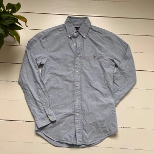 Ralph Lauren skjorta - Säljer en stilren ljusblå skjorta från Polo Ralph Lauren i storlek S. Skick 10/10! Skjortan är i slim fit och har långa ärmar med knappar. Den är tillverkad i bomull och har en broderad logga på bröstet. Perfekt för både vardag och fest! 💙