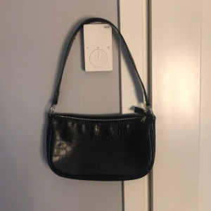 Svart axelväska med krokodilmönster - Snygg svart axelväska i syntet med krokodilmönster och dragkedja. Perfekt för att ge din outfit en trendig touch. Enkel att bära med en bekväm axelrem.