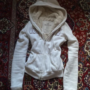 Vit hoodie från Hollister - Mysig vit hoodie från Hollister med mjukt foder och dragkedja framtill och nedantill. Perfekt för kyliga dagar!