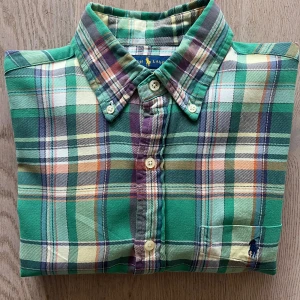 Grön rutig skjorta från Ralph Lauren - Snygg grön rutig skjorta från Ralph Lauren i klassisk passform. Skjortan har långa ärmar och knappar framtill. Perfekt för en stilren look med en touch av färg.