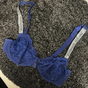 Spets-BH från Victoria's Secret - Säljer en snygg blå BH från Victoria's Secret med spetsdetaljer och justerbara axelband. Perfekt för att känna sig både bekväm och stilren. Axelbanden har märkets logga för en extra touch av lyx.
