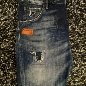 Blå jeans från Dsquared2 - Storlek 32. Snygga blå jeans från Dsquared2 med slitna detaljer och en cool, vintage look. De har en klassisk femficksdesign och en läderpatch med logotyp på baksidan. Perfekta för en avslappnad stil. Pris kan diskuteras vid snabb affär
