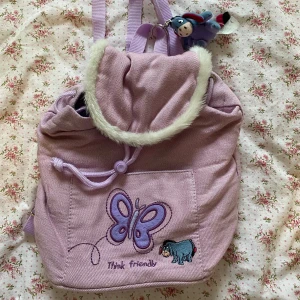 Vintage ryggsäck från USA  - Supersöt liten ljuslila ryggsäck med broderad fjäril och Ior från Nalle Puh. Väskan har en fluffig kant och justerbara axelremmar. Väskan skall vara från 90-talet och köpt i USA! Köptes för ca 350kr med frakt, aldrig använt. 
