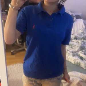 Blå pikétröja från Ralph Lauren - Säljer en klassisk blå pikétröja från Ralph Lauren med den ikoniska rosa loggan på bröstet. 🩷