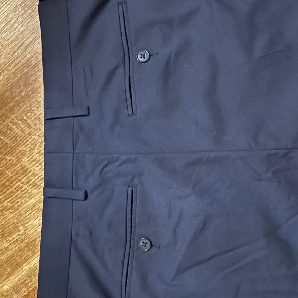 Snygga mörkblå kostymbyxor från Riley. Byxorna har en klassisk design med knappar och bälteshällor, perfekta för en stilren look. Avslappnad passform. Endast använda två gånger. . Farkut & Housut.