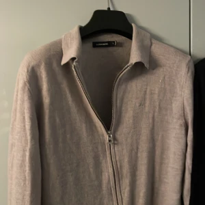 Grå tröja med dragkedja från J.Lindeberg - Säljer en stilren grå tröja från J.Lindeberg med dragkedja framtill. Tröjan har en diskret logga på bröstet och är tillverkad i ett mjukt material. Perfekt för en avslappnad look. Hör av er om ni vill diskutera priset!!!