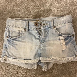 Ljusblå jeansshorts från Lab Industries - Snygga ljusblå jeansshorts från Lab Industries med slitna detaljer och fransar vid bensluten. Shortsen har en knapp och dragkedja framtill samt fem fickor. Perfekta för en avslappnad stil.26cm lång,tvärs över 36