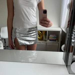 Silver paljettkjol från Weekday - Snygg silverfärgad paljettkjol från Weekday med en stilren slits på sidan. Perfekt för att glittra till din outfit. Kjolen är kort och har en tight passform som framhäver figuren. Ett måste för den som älskar att sticka ut!