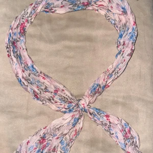 Blommig halsduk i ljusa färger - Säljer en lätt och luftig halsduk med ett vackert blommönster i rosa och blått på en ljus bakgrund. Perfekt för att ge en färgklick till din outfit.