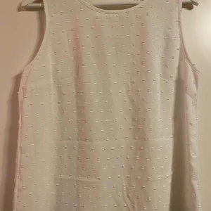 Vit ärmlös topp med spetsdetaljer - Säljer en söt vit ärmlös topp med mönster och vacker spets längs ryggen. Strl M och fint skick! 