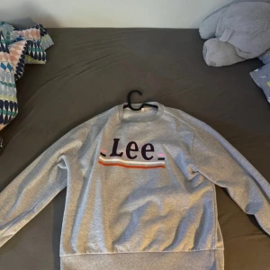 Grå sweatshirt från Lee - Säljer en grå sweatshirt från Lee med färgglada ränder och logotyp på framsidan. Tröjan har långa ärmar och en bekväm passform. Perfekt för en avslappnad stil.