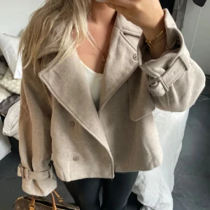 Beige kappa - Säljer en stilren beige kappa med knappar framtill. Jackan har en klassisk design med långa ärmar och en bred krage. Perfekt för att hålla stilen i höst och vår🤎🤎