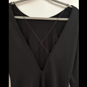 Svart klänning från Only - Snygg svart klänning från Only med långärmad design och djup v-ringning. Klänningen har en stilren look med korsade band i ryggen som ger en extra touch. Perfekt för en kväll ute eller en speciell tillställning.  Mått:  Byst: 42 cm Midja: 35 cm Längd: 82 cm Innerärm: 51 cm