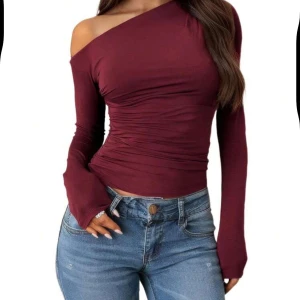 Vinröd oneshoulder topp - Snygg vinröd oneshoulder topp med lång ärm. Perfekt för en trendig look, den har en tight passform som framhäver figuren. Tillverkad i ett mjukt och stretchigt material för extra komfort. Aldrig använd