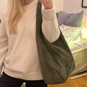 Olivgrön axelväska i mocka - Sjukt najs olivgrön axelväska i äkta mocka. Väskan har en enkel design med en bred axelrem som gör den bekväm att bära. Perfekt för att rymma alla dina vardagliga nödvändigheter. 