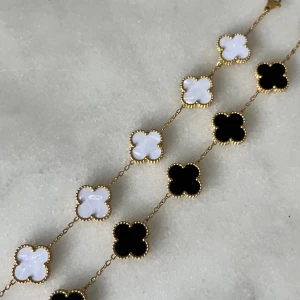 Halsband med fyrklöverdesign - Elegant armband  med fyrklöverformade hängen i svart och vit. En kostar 150kr helt nya aldrig använd, gjort av guld pläterat rostfritt stål 